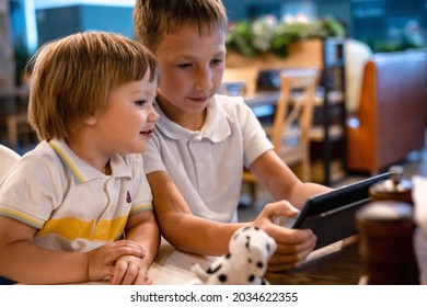 Boy and toddler playing video games on tablet online on internet while waiting orders in restaurant. Children using smartphone. Kids using technology. Screen time addiction.