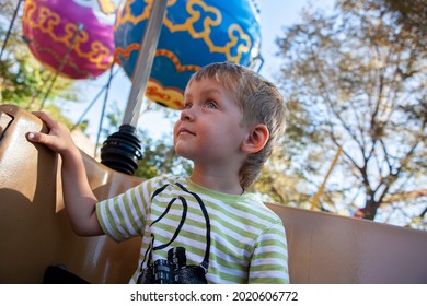 Boy toddler sits at a booth in the carrousel. Happy baby is at at amusement park . Smiling boy rides art attraction in a fairground. Leisure with family.