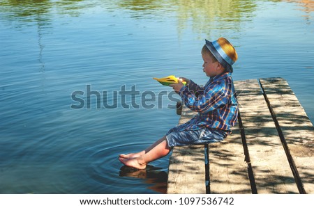 Boy with toy ship or boat on old wooden pier or dock on the lake. Summer vacation and healthy lifestyle concept. Kid having fun outdoors. having fun on summer vacation. Holiday travel concept