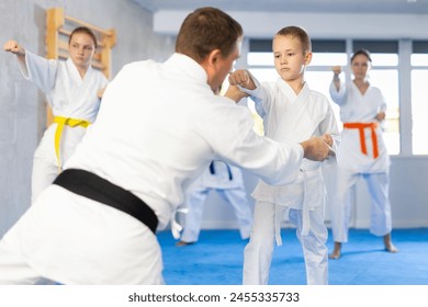 Boy train and learn during family group lesson in oriental martial arts. Man teacher corrects pose posture position of body, hands during karate classes. - Powered by Shutterstock