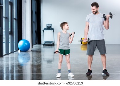 Boy training with dumbbells together with coach at fitness center - Powered by Shutterstock