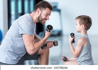 Boy Training With Dumbbells Together With Coach At Fitness Center