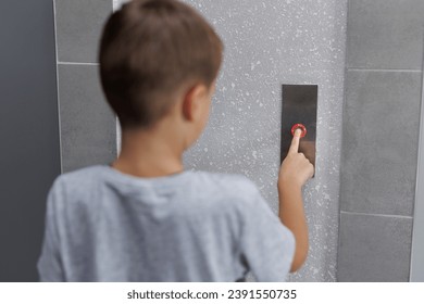 Boy tries to push the elevator button up and down. Child stretches out his hand and finger to press the button
