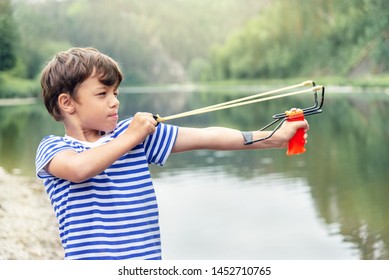 boy in a t-shirt on the background of nature holding a slingshot