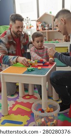 Boy and two men stacking colorful plastic blocks on a low play table in a building playroom with toy shelf and foam mat; bonding joy together.