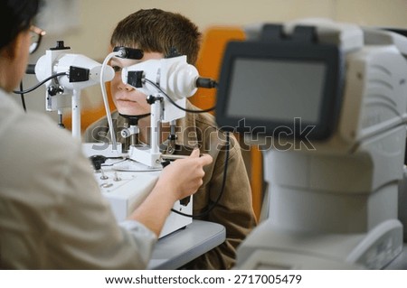 Boy undergoing vision diagnostics with innovative equipment operated by ophthalmologist in clinic