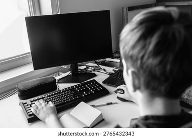 Boy using desktop computer at home workspace black white