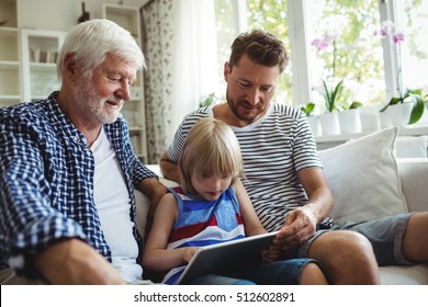 Boy using digital tablet with his father and grandfather in living room at home - Powered by Shutterstock