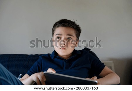 Boy using digital tablet at home for online learning, social media, video streaming, and entertainment. Modern childhood technology, screen time, internet use, education, and family lifestyle concept.