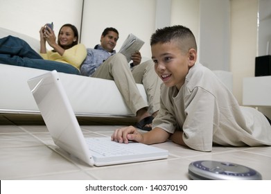 Boy using laptop on floor with mother and father on sofa in the living room at home