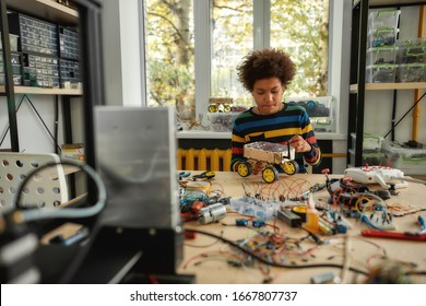 Boy Using Screwdriver While Fixing Bolts On A Robot Vehicle. Smart Kids And STEM Education. Robotics And Software Engineering For Elementary Students.