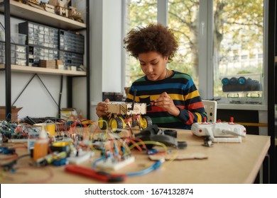 Boy Using Screwdriver While Fixing Bolts On A Robot Vehicle. Smart Kids And STEM Education. Robotics And Software Engineering For Elementary Students.