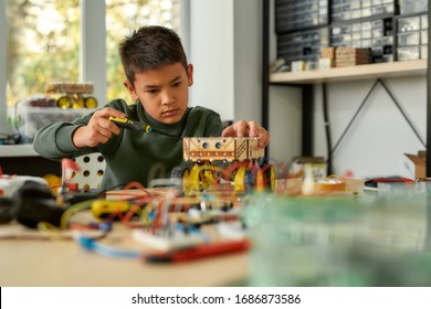 Boy Using Screwdriver While Fixing Bolts On A Robot Vehicle. Smart Kids And STEM Education. Robotics And Software Engineering For Elementary Students. Selective Focus