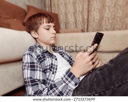 Boy using smartphone on couch at home. Pre-teen boy lying on sofa and scrolling smartphone screen, addicted to social media and gadgets. Modern childhood and screen time concept.