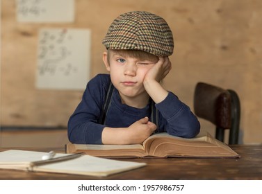 a boy in vintage clothes sits at a table with books, he is bored, he makes faces and wants to sleep
