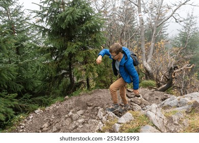 Boy walking along steep and rocky mountain path on misty day, dressed in blue puffer jacket with a backpack. Adventure travel, physical challenge, and exploring the great outdoors in foggy conditions - Powered by Shutterstock