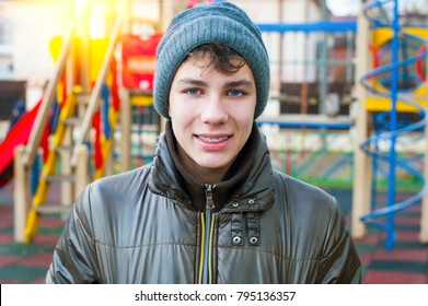 A Boy In A Warm Cap And Jacket With Braces On His Teeth Walks Around A Playground With A Younger Brother In Winter