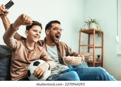 Boy watching soccer match with father at home, sitting on sofa - Powered by Shutterstock