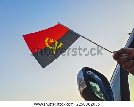 Boy waving Angola flag against the blue sky from the car window close-up shot. Man hand holding Angolan flag, Copy space 