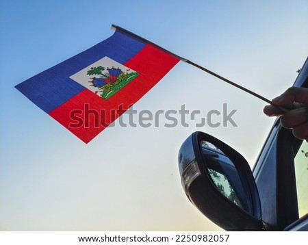 Boy waving Haiti flag against the blue sky from the car window close-up shot. Man hand holding Haitian flag, Copy space 