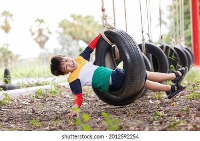 A boy wearing bright colored clothes playing tire swing hanging at playground and having fun healthy summer vacation activity.