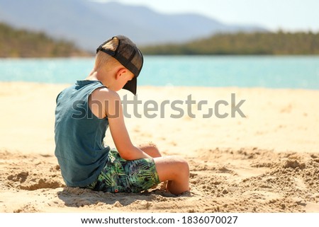 Boy wearing cap sitting on beach playing in sand
