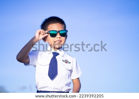 A boy wearing dark glasses in a pilot suit on a blue tone background.