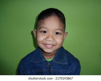 Boy Wearing Jeans Sitting, Smiling, Showing Teeth, Happy, Staring At The Camera. Green Background