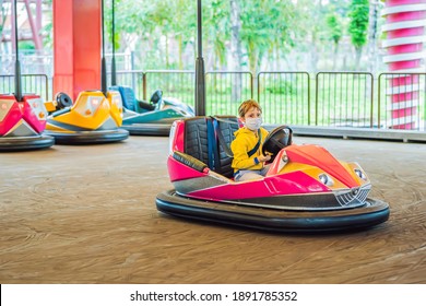 Boy Wearing A Medical Mask During COVID-19 Coronavirus Having A Ride In The Bumper Car At The Amusement Park