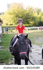 A Boy Wearing Orange Shirt And A Helmet Sitting On Top Of A Small Black Horse