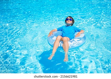 Boy wearing sun glasses, relaxing on an inflatable swim ring in a sunny day, spending time in a swimming pool, aquapark resort hotel. Summer holidays concept. - Shutterstock ID 2156621981