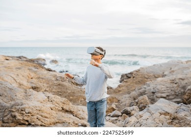 Boy Wearing Virtual Reality headset simulator on a rock breakwater, by the sea - Powered by Shutterstock