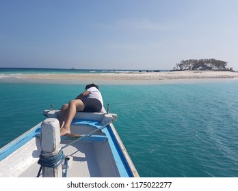 Boy Wearing White Tee Shirt , With Face No Seen, Lays Down On The Wooden Boat Deck Anchored In Front Of Empty Sand Island With The Tree