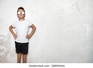 Boy wearing white tshirt, shorts stands on a wall background of  and smiling