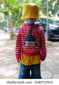 A Boy Wearing Yellow Hat And Red Jacket In Garden