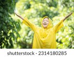 A boy wearing a yellow raincoat. Happy Asian little child having fun playing with the raindrops. A boy looking up at the sky and enjoying rainfall.