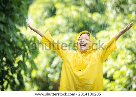 A boy wearing a yellow raincoat. Happy Asian little child having fun playing with the raindrops. A boy looking up at the sky and enjoying rainfall.