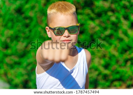 a boy in a white T-shirt and black glasses punches forward with his fist