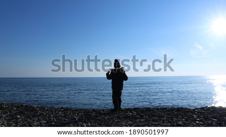 a boy in winter clothes standing facing the sea rejoices at a coastal walk, a silhouette of a young man on a rocky coast of the winter sea, one child against the background of a blue cold sea