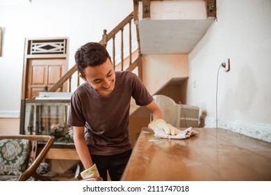 A boy wipes a wooden cupboard while cleaning the house