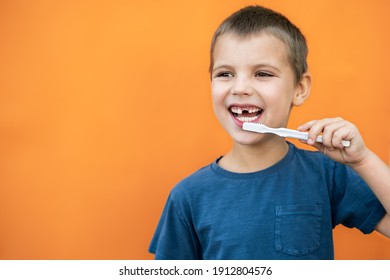 Boy without milk upper tooth in blue t-shirt holds toothbrush in hand on the orange background. Copy space. - Powered by Shutterstock