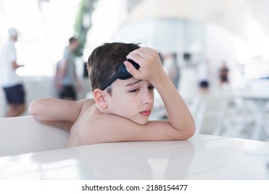 A Boy Without A T-shirt Is Sitting In A Cafe On Vacation And Waiting For A Waiter, Sad. Swimming Goggles On His Head