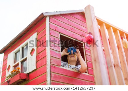 Boy in a wooden playhouse looking through a binocular