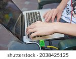 The boy is working on a computer on his lap . A cute Caucasian boy sitting on the bench in the park with his laptop on his knees and laughing