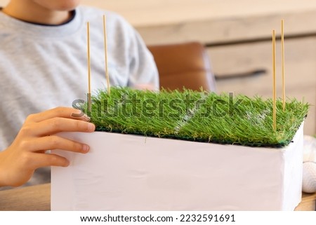 Boy workshop school project create soccer field with artificial grass, school assignment creative handcraft from a carton board,  Creative hobby making handcraft toy football field at home.
