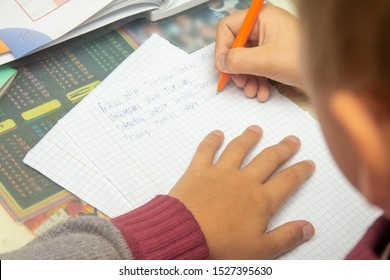 A boy writes English words by hand on traditional white paper in a notebook. The boy writes his first test on English. Child writing, spelling and education. Boy learns english. English writing skills