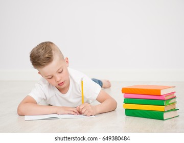 Boy writes in a notebook while lying on the floor of the house