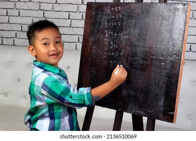 A boy is writing on a blackboard with a chalk.