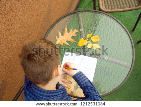 Boy is writing something. Boy is doing homework outdoors. Boy is drawing on paper or writing a letter