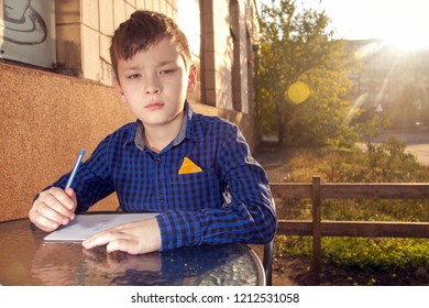 Boy wrtitting something. Boy doing homework outdoors. Boy drawing on paper or wrtitting a letter